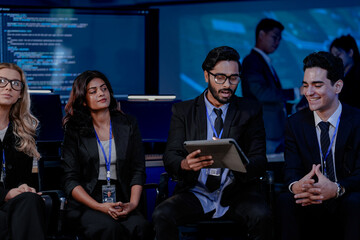 Obraz premium A large IT department meeting in a command center (SOC). An Indian analyst holds a tablet, listening with his team to a cybersecurity update on an AI system.
