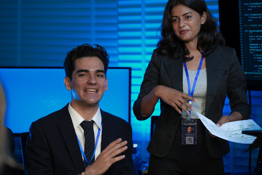 An Indian female developer leads a code review, holding a report. She explains a Python script for an AI or cybersecurity system to her team in a dark SOC Security Operations Center.