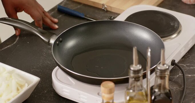 African man tilting pan on white hotplate heating oil, dropping onion rings into oil on countertop