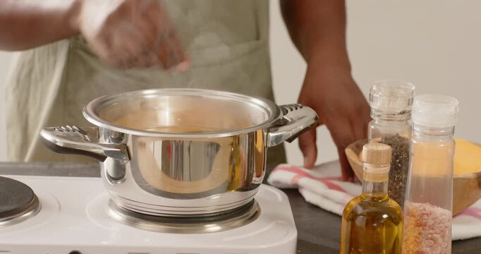 African American man in apron, pot boiling, adding orange spice and stirring for flavor on hotplate