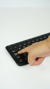 vertical position of a woman's index finger pressing the Caps Lock key on a black wireless keyboard, isolated on a white background,