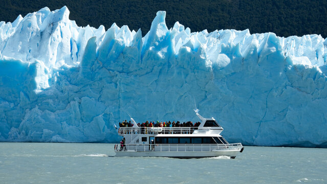 Tourist boat navigating near a massive glacier with blue ice formations in cold glacial water in Patagonia, Argentina