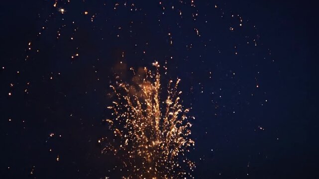 A vibrant golden firework burst exploding in a kaleidoscope of glowing sparks and trails against a dark black night sky during a festive celebration or holiday event at night.