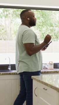 Vertical video: Tapping phone, man in tee speaking into earbuds in kitchen, checking laptop on call