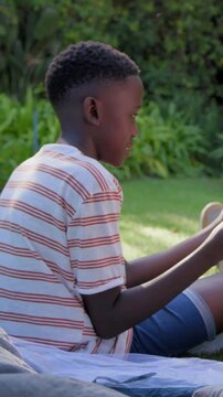 Vertical video: Checking tin cup, boy in striped T glancing off-frame drinking on blanket in garden