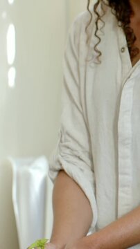 Vertical video: Pulling back shot showing grower in linen top potting seedling at home, copy space