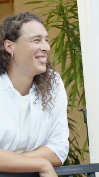Vertical video: Seeing offscreen guest, person smiling and leaning on railing on porch, white shirt