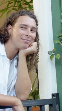 Vertical video: Reacting to offscreen cue, nonbinary adult in white tee leaning on gate at door