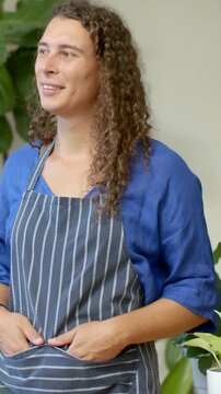 Vertical video: Smiling after cue nonbinary person adjusting striped-apron among plants in blue top