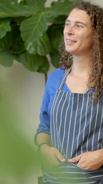 Vertical video: Hearing off-frame voice, cook in striped apron smiling at cafe by plant, copy space