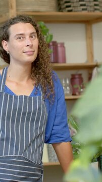 Vertical video: Leaning staff tilting after off-frame voice at plant shop counter, in striped apron