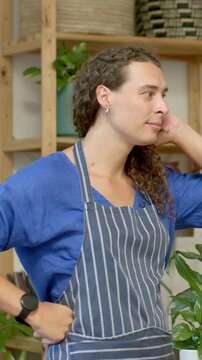 Vertical video: Hearing cue, plant florist in striped apron turning, touching ear, reaching plant