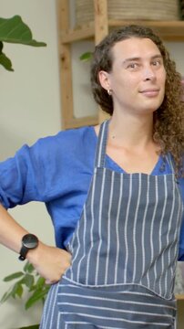 Vertical video: Shifting chef adjusting pose while camera rolling in kitchen, with apron for camera