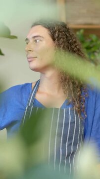 Vertical video: Noticing plants, florist turning and scanning in plant shop wearing striped apron