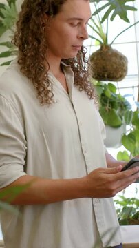 Vertical video: Checking messages on phone adult in beige shirt scrolling by window plants