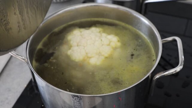 Stockholm, Sweden A whole head of cauliflower boils in a pot of vegetable bouillon on a stove. 