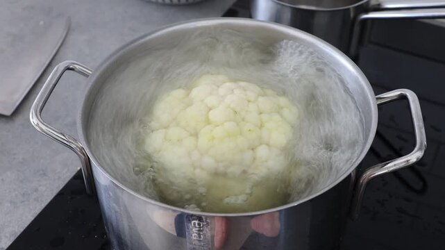 Stockholm, Sweden A whole head of cauliflower boils in a pot of vegetable bouillon on a stove. 