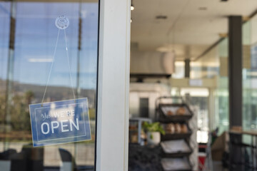 Naklejka premium Yes WE'RE OPEN sign is hanging on glass door with dotted chain, blurred bakery interior