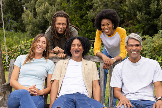 Five friends sitting laughing on wooden swing bench with metal chains in garden with wristwatch