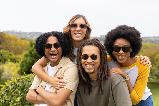 Diverse friends posing on park hill, wearing sunglasses, wristwatch, bracelet, hugging