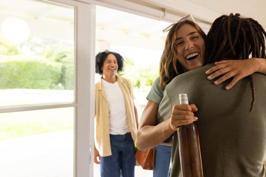 Couple hugging while woman holding sealed wine bottle and wearing sunglasses at doorway, copy space