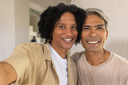 African American male friends taking selfie with phone, wearing beige shirts and sunglasses in hall
