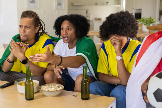 African American friends watching, reacting to TV showing goal in living room with soccer ball
