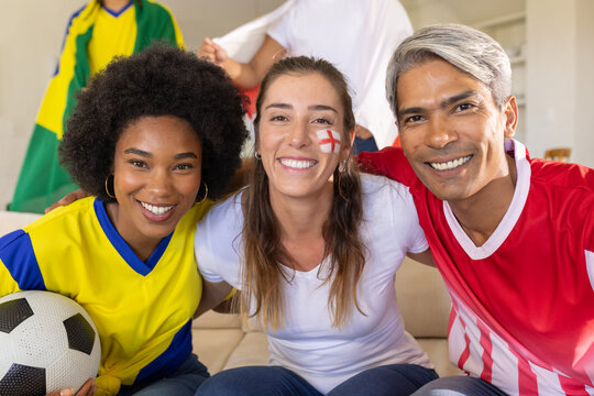 Friends wearing team jerseys cheering and posing on couch at home after goal, holding soccer ball