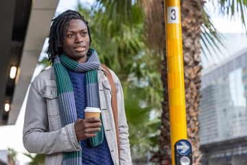 Mid-adult African American man standing on sidewalk holding paper cup wearing denim jacket scarf © wavebreak3