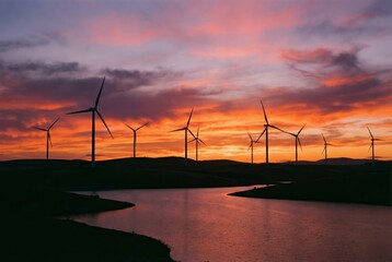 Obraz premium Silhouette of wind turbines over water at vibrant orange and purple sunset