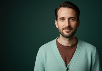 Obraz premium Professional Portrait of a Man Wearing a Mint Green Cardigan and Brown Shirt Looking at Camera with Friendly Expression Against a Dark Forest Green Background