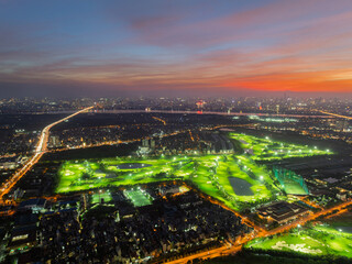 Obraz premium Aerial night view of a brightly lit golf course in Long Bien district, Hanoi, highlighting fairways, water hazards, road network, and surrounding residential areas.