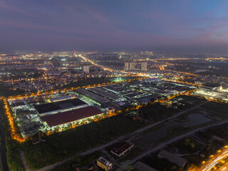 Obraz premium Night aerial view of a brightly lit industrial zone in Long Bien district, Hanoi, highlighting factory operations, road networks, and surrounding urban expansion.