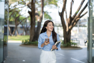 Asian woman walking, holding book and smartphone © Apichat