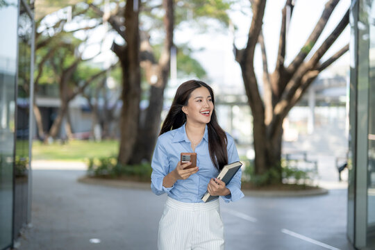 Asian woman walking, holding book and smartphone