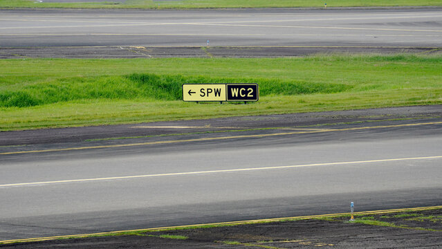 Airport taxiway directional signs SPW and WC2 located on the grass field side for aircraft pilot navigation and ground control.