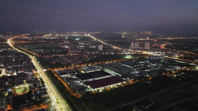 Aerial night view of an industrial area in Long Bien district, Hanoi, with illuminated factories, busy road intersections, and dense surrounding urban neighborhoods.