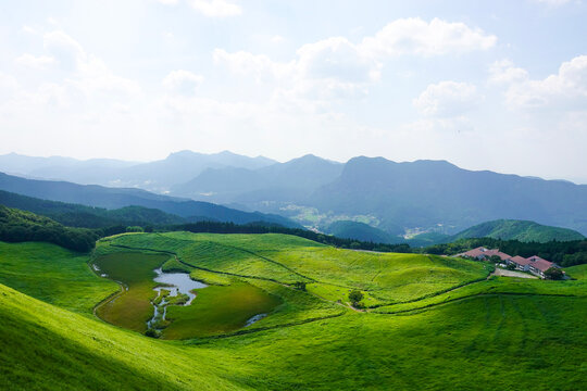 Panoramic summer view of Soni Kogen featuring lush green rolling hills, a small pond, and distant mountain ranges