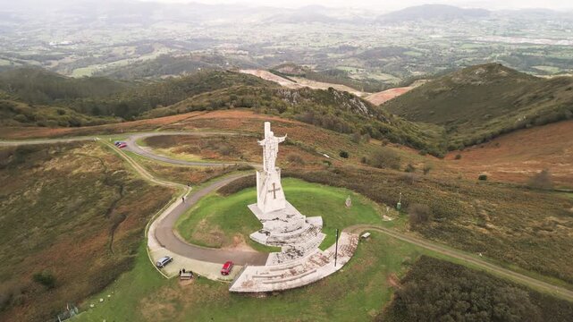 Epic Jesus Christ monument mountain landscape aerial pull-back. 
Cinematic drone reveal flight from ancient Sagrado Corazon statue 
on Monte Naranco peak to green valley hills in Oviedo Spain.
