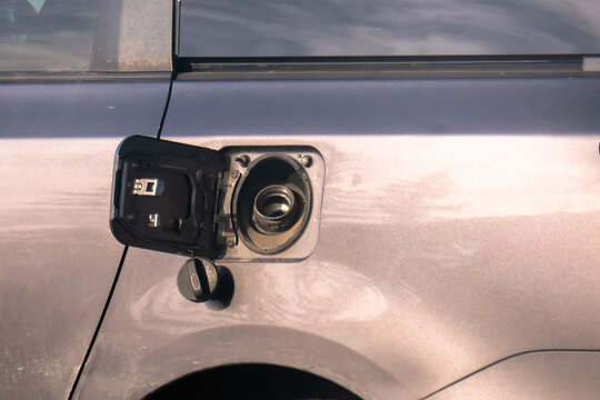 Close-up of an open fuel filler door on a dusty grey car with the gas cap hanging down. Concept of refueling, energy, or vehicle maintenance.