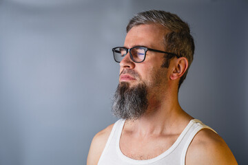 Casual man with beard and glasses posing in studio Man with beard and glasses stands in front of gray background © mykhailo
