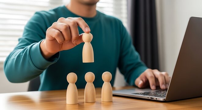 Businessman selecting individual wooden figure representing leadership and recruitment strategy at desk with laptop