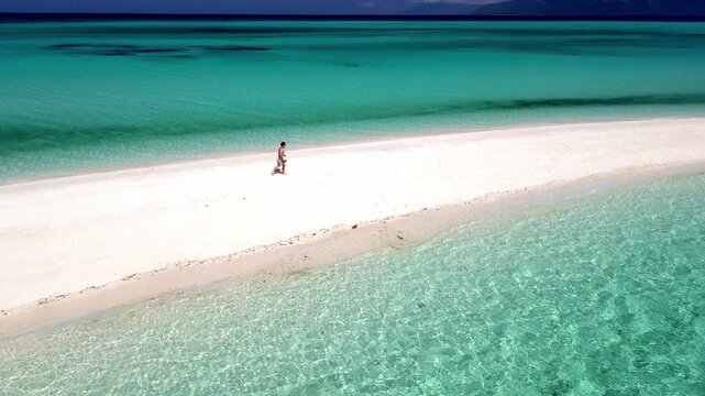Drone shot of a person walking on a pristine white sandbar surrounded by turquoise water.