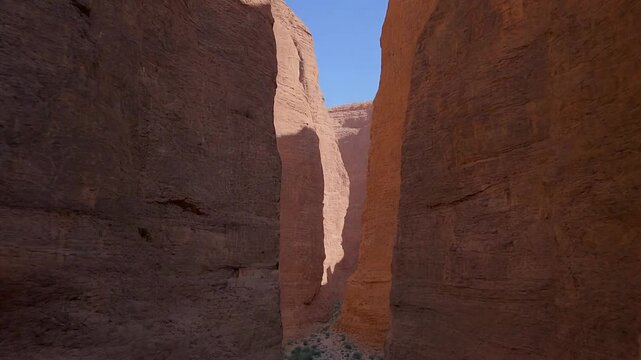 A scenic view of a narrow canyon with tall red rock formations under a clear blue sky.
