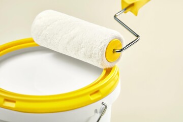 Obraz premium Paint roller resting on the edge of a white paint bucket with yellow rim