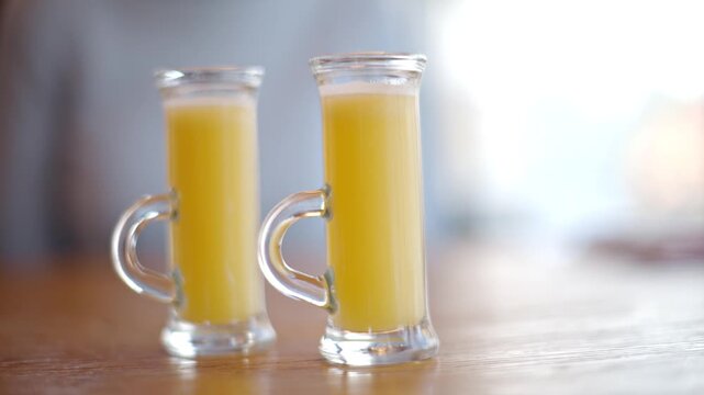 Limoncello shot glasses on wooden table in bright cafe setting with smooth cinematic camera panning.