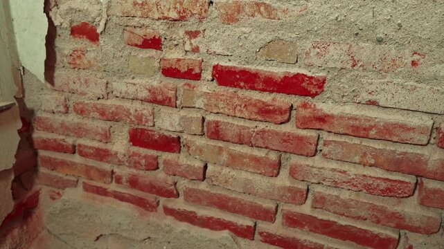 Exposed rough red brick wall with crumbling plaster and mortar