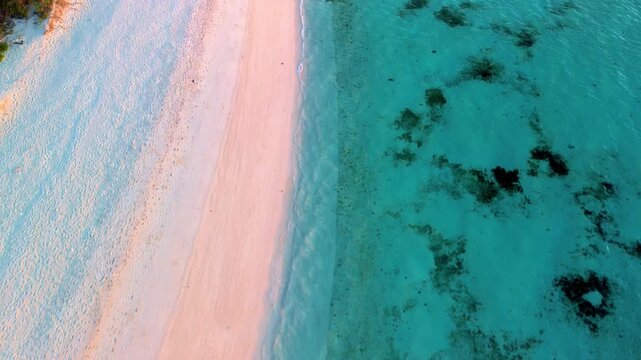 Top-down aerial view of a pristine white sand beach meeting clear turquoise tropical waters with visible coral patches.