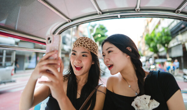 Live streaming on smartphone two young woman sisters gen Z influencer sitting tuk tuk taxi local tour travel
