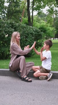 Vertical video. Joyful interaction. Childhood fun. Happy mother cheerful son playing in green park enjoying hand clap game summer family leisure outdoor.